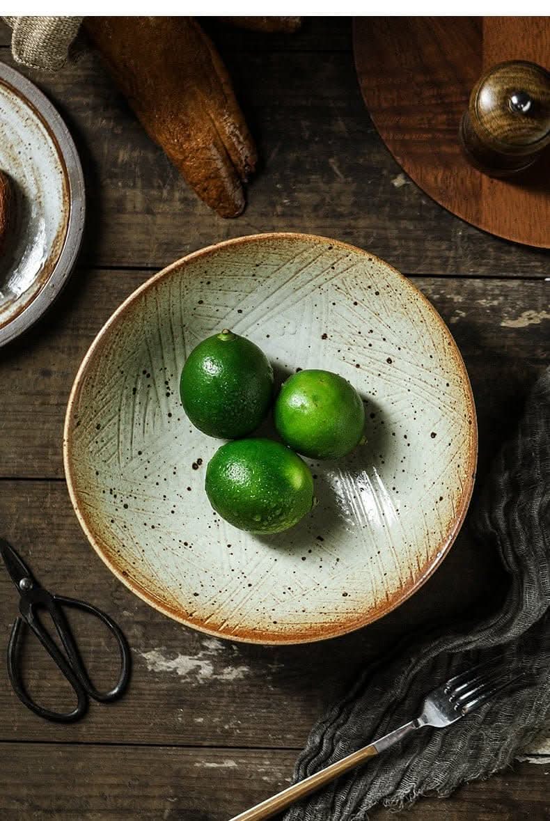 Tripod Stoneware Fruit Plate with limes on rustic wooden table, next to scissors and fork.